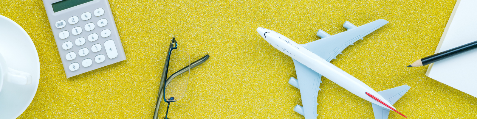 calculator, glasses, model airplane, paper and pencil scattered on table'